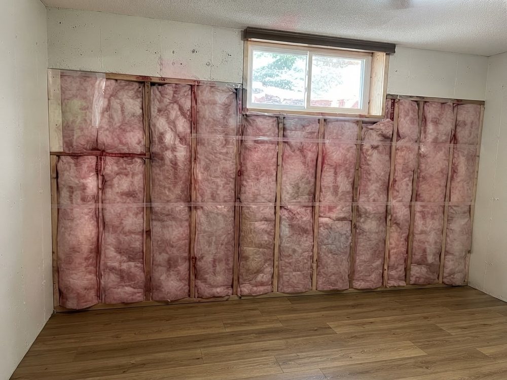 Basement wall framing with fresh pink insulation installed between the studs
